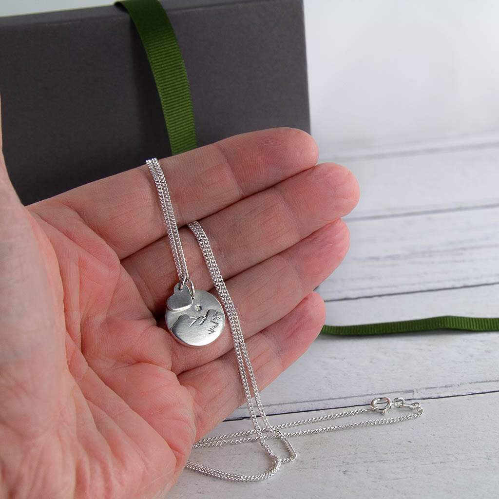 Silver necklace of Catbells held in a hand on a wooden surface