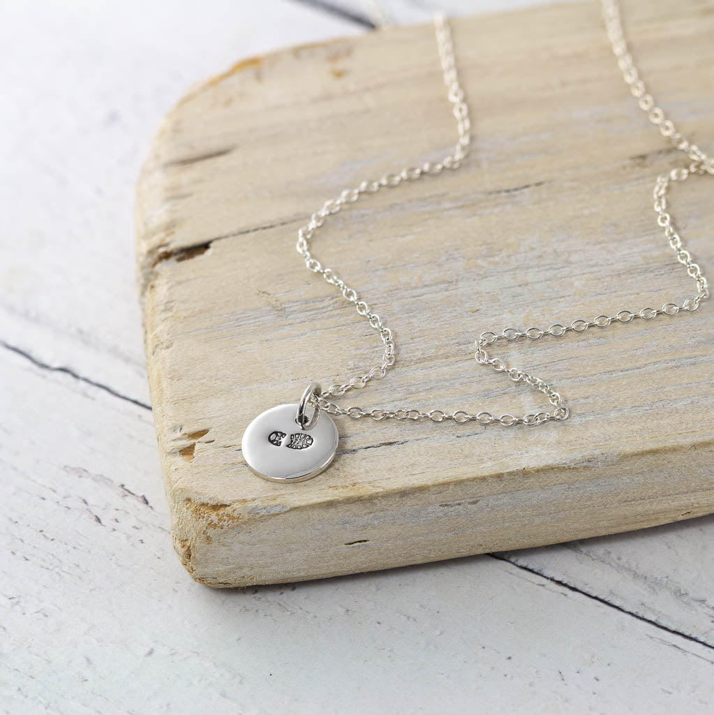 silver necklace stamped with a hiking boot load on a wooden block