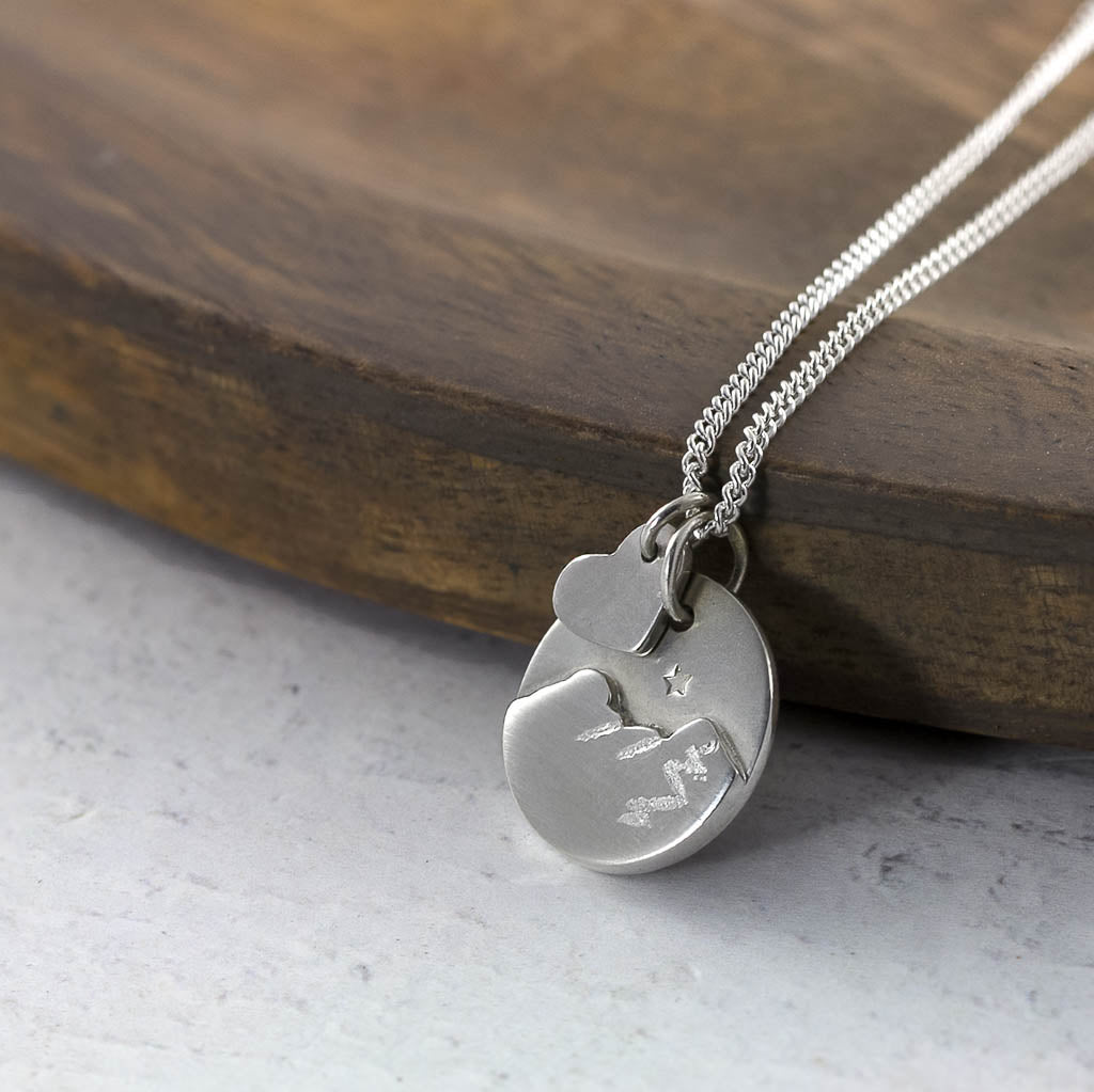 Silver necklace with a round pendant Of Catbells in the Lake District, on a wooden surface